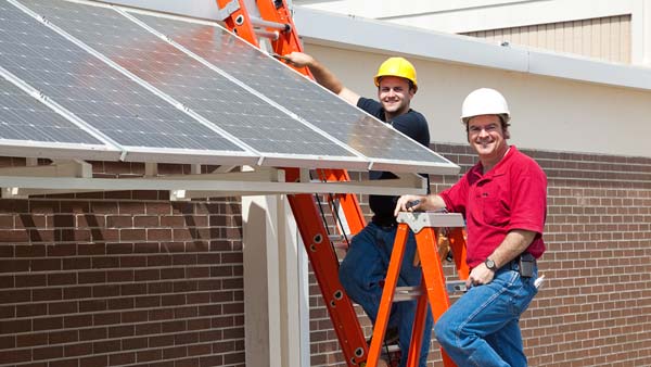 Two men on ladders installing solar panels 